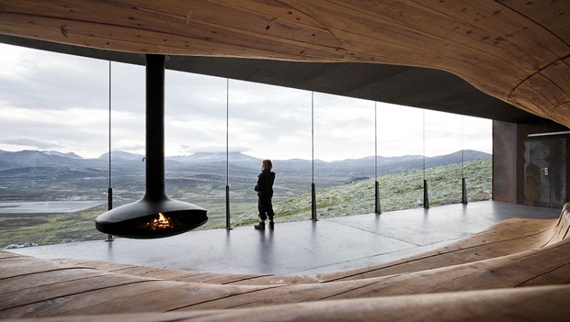 木材以流動的線條延展出3 階座位，天花 板垂吊的火爐給人溫厚的暖意。（圖片來源：Ketil Jacobsen）
