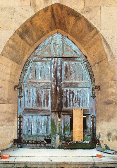 教堂玻璃窗上充斥著大小不一的洞，木門的油漆已經脫落大半。